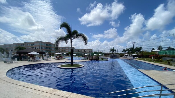 A swimming pool area with a palm tree, lounge chairs, and umbrellas. - Flat 110 Muro Alto CC by LaPlaya (Ipojuca)