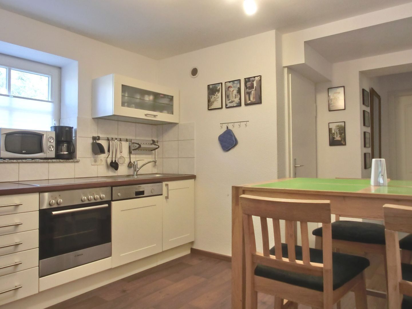 A compact kitchen with white cabinets, a microwave, a Bosch oven, and a wooden dining table with chairs.