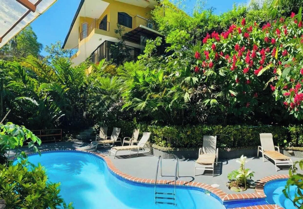 A swimming pool with lounge chairs and a yellow building in the background.