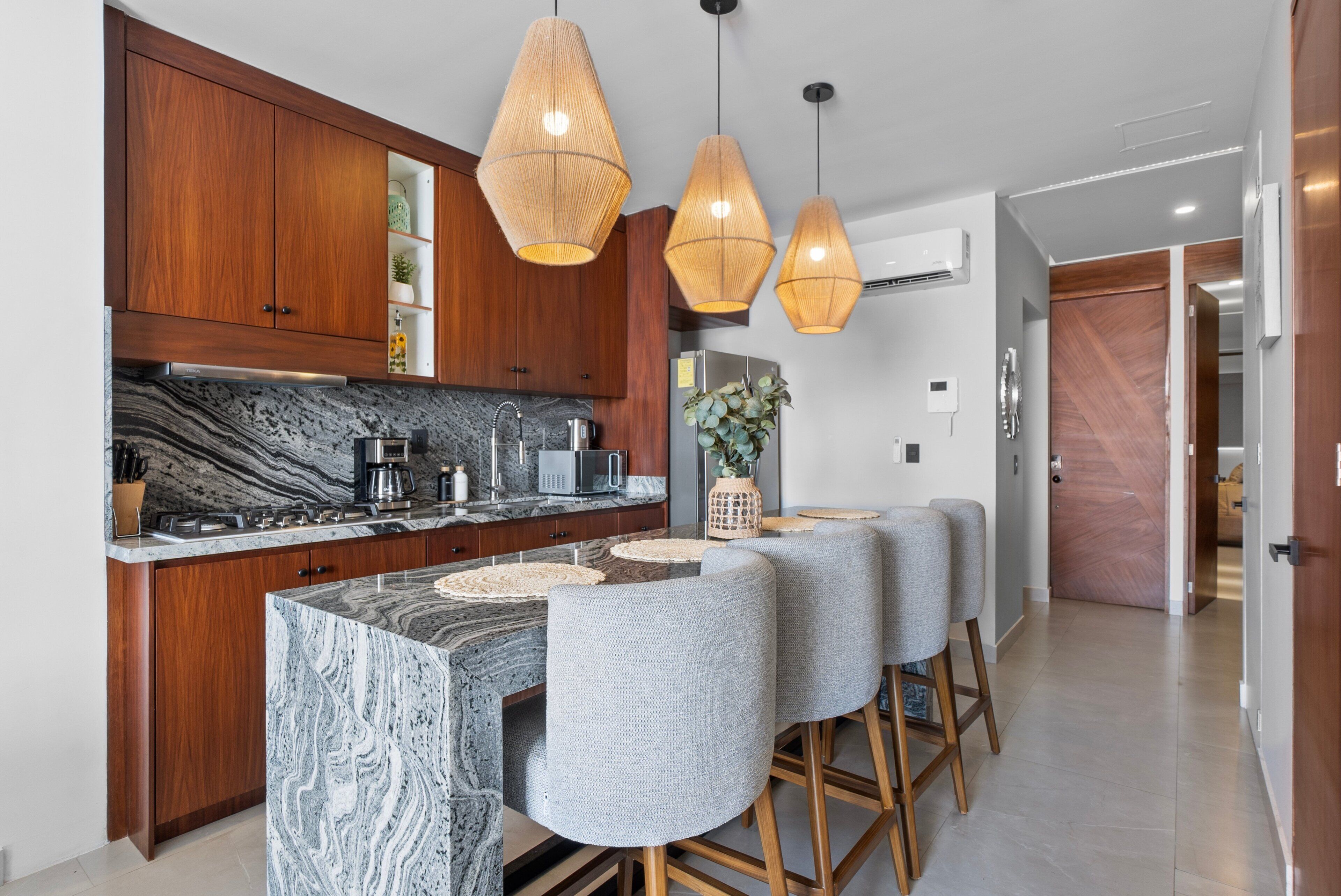 A modern kitchen with wooden cabinets, a marble island, and a bar area with stools.