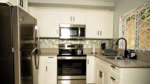 A modern kitchen with stainless steel appliances, white cabinetry, and a tiled backsplash. - North Ritz Villa - 1 Bedroom Apartment (Ocho Rios, Draxhall, St Ann, Jamaica)