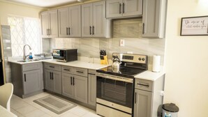 Una cucina moderna con mobili grigi, elettrodomestici in acciaio inossidabile e una parete di fondo rivestita di piastrelle.