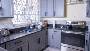 A modern kitchen with grey cabinets, a stainless steel oven, and a window with a diamond-patterned screen.