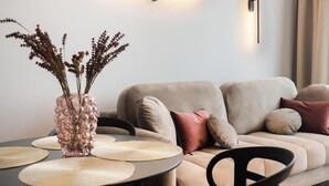 Ein modernes Wohnzimmer mit einer Couch, einem Esstisch mit Stühlen, einer Vase mit Trockenblumen und einer Pendelleuchte.