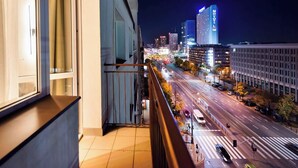 Nachtansicht einer Stadt vom Balkon mit Blick auf eine belebte Straße und hohe Gebäude.