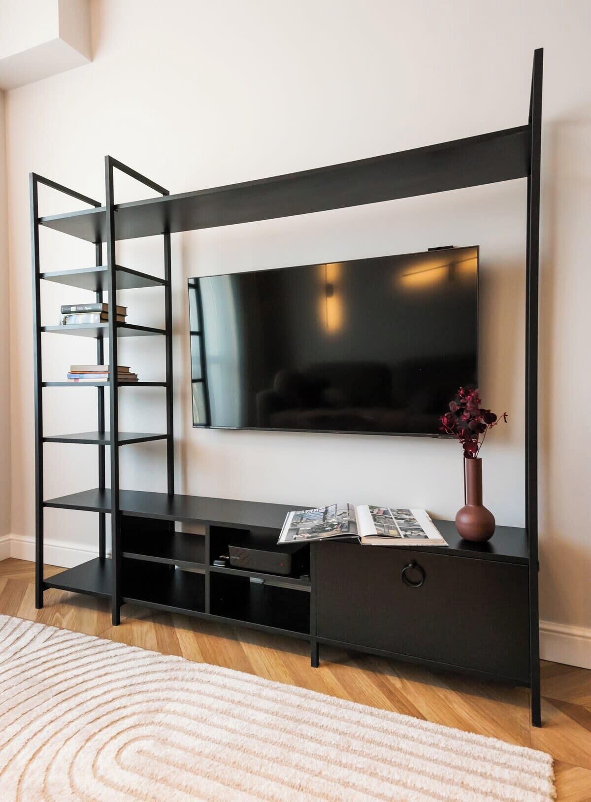Un salon moderne avec un meuble de rangement noir pour les appareils électroniques, un téléviseur à écran plat fixé au mur et une petite table d’appoint sur laquelle est posé un vase.