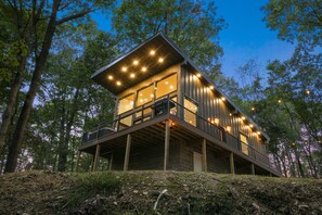 A modern wooden cabin with a balcony, surrounded by trees.