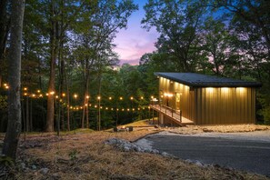 Une cabane dotée d’une terrasse, entourée d’arbres et illuminée de guirlandes lumineuses.