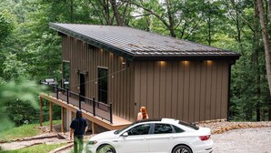 A small, single-story building with a metal roof and a wooden deck. - Ridgeview | Hocking Hills, Luxury Cabin, Hot Tub (Rockbridge)