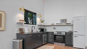 A modern kitchen with dark cabinets, a white refrigerator, stainless steel appliances, and a window with a view of trees. - Ridgeview | Hocking Hills, Luxury Cabin, Hot Tub (Rockbridge)
