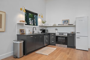 A modern kitchen with dark cabinets, a white refrigerator, stainless steel appliances, and a window with a view of trees. - Ridgeview | Hocking Hills, Luxury Cabin, Hot Tub (Rockbridge)