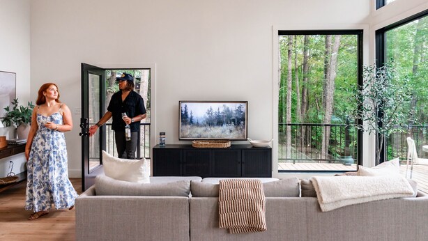 A modern living room with a large window, a sofa, a television, and a dining area. - Ridgeview | Hocking Hills, Luxury Cabin, Hot Tub (Rockbridge)