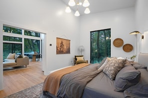 A modern bedroom with a large bed, a view of the outdoors, and a dining area with a table and chairs.
