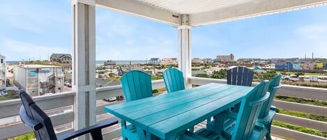 Une terrasse couverte, dotée d’une table et de chaises, qui offre une vue sur une ville côtière.