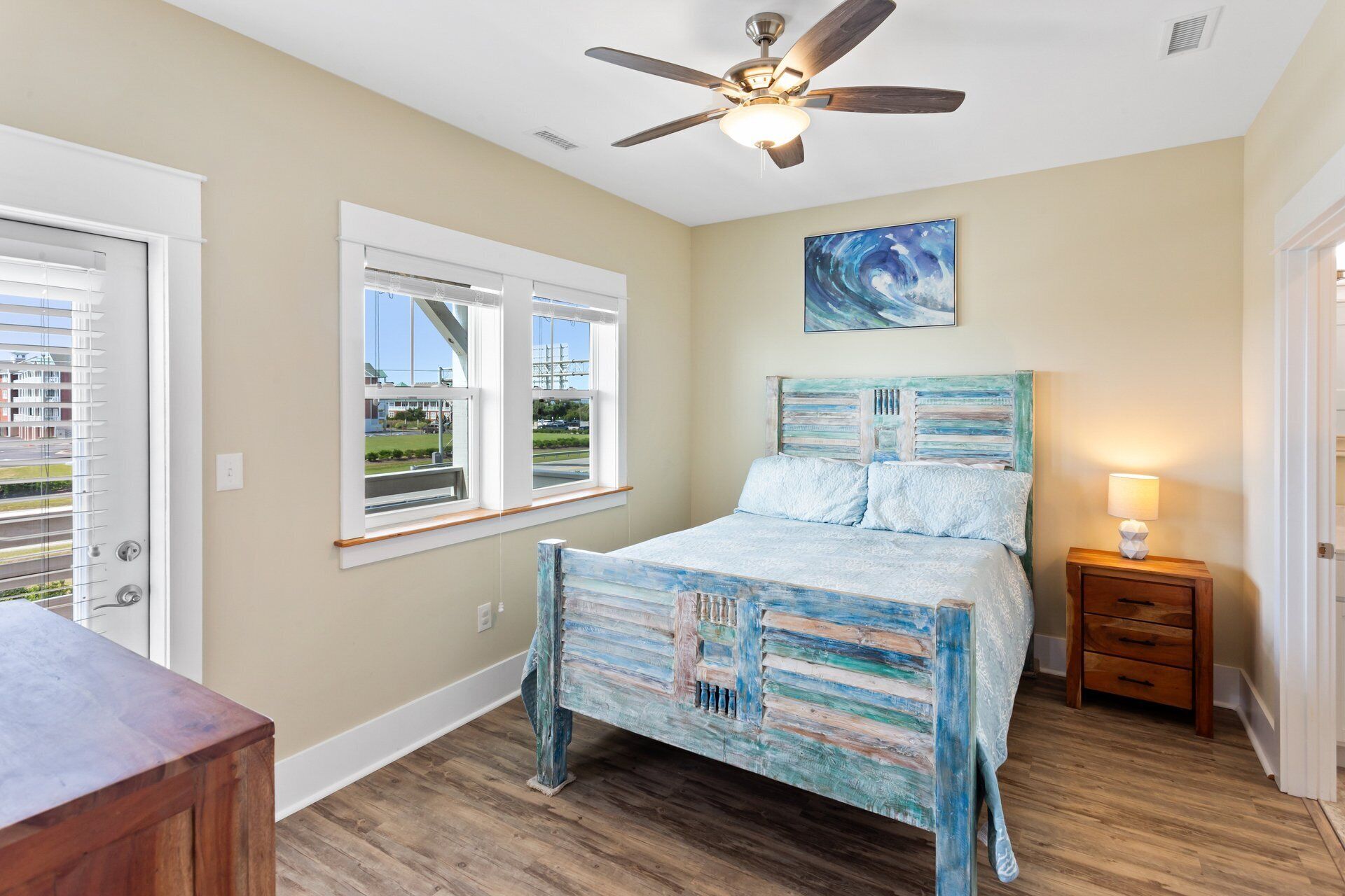 A bedroom with a bed, a ceiling fan, a window, and a painting on the wall.