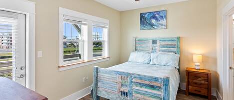 A bedroom with a bed, a ceiling fan, a window, and a painting on the wall.