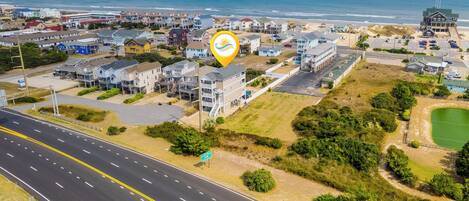 An aerial view of a coastal town with a road running through it, buildings, and a beach in the background.