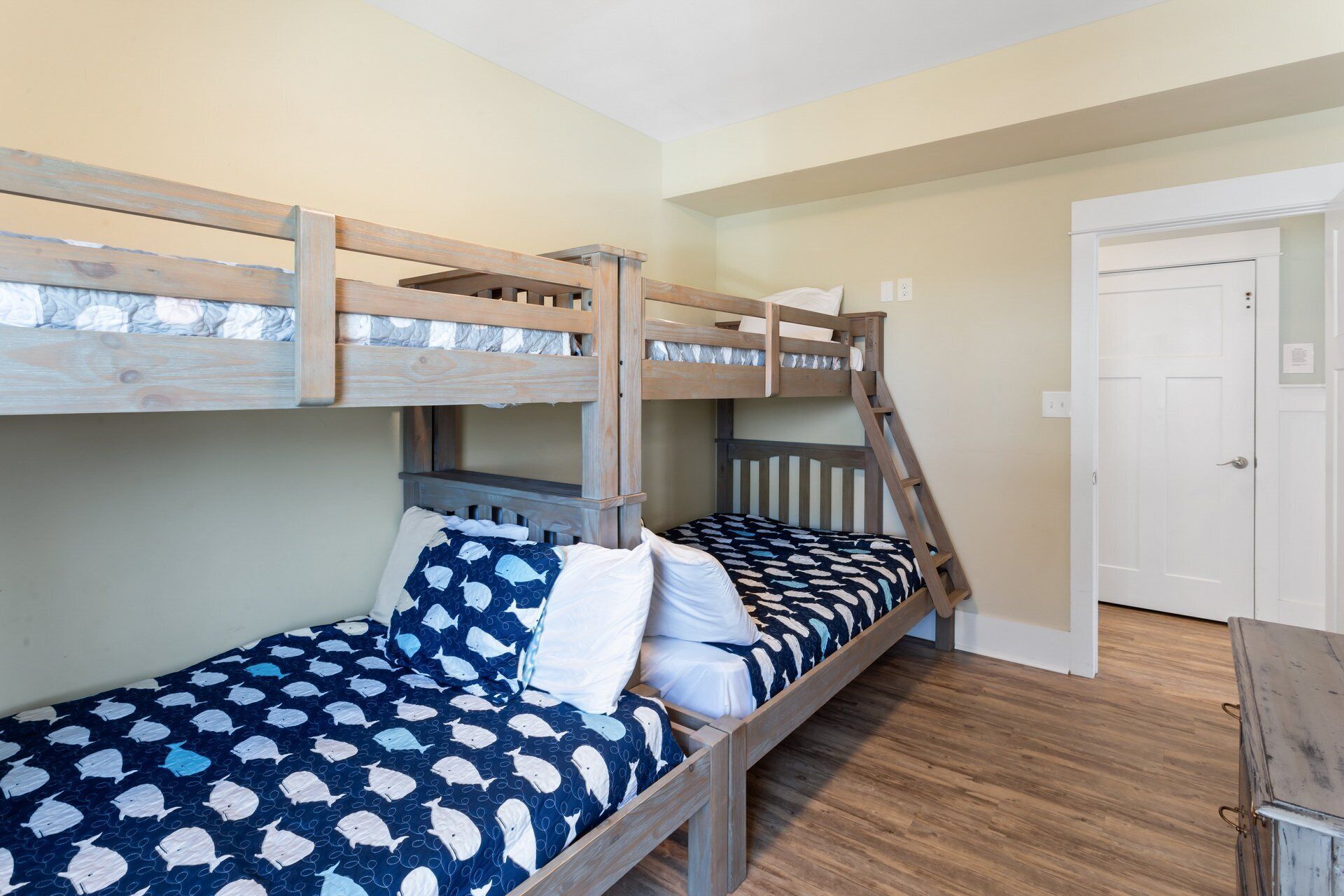 A bunk bed room with a wooden ladder, a door, and a small wooden chest.