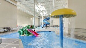 Un parc aquatique intérieur doté d’une grande sculpture de grenouille, d’un toboggan aquatique et d’une fontaine.