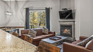 Un salon avec une cheminée, un téléviseur et une vue sur les arbres à l’extérieur.