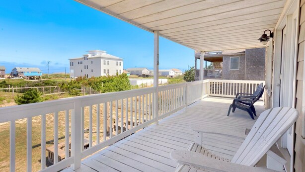 A covered porch with white railings, two lounge chairs, and a view of beach houses and the ocean. - Shorely Bliss 3-Min Walk to Beach w/ Hot Tub (Kitty Hawk)