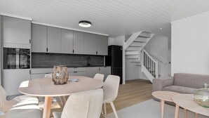 A modern kitchen with grey cabinets, a black refrigerator, and a built-in oven. There is a dining area with a round table and chairs, and a staircase leading to another level. - 4 bedroom lovely home in Risør (Risør)