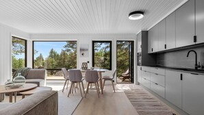 A modern kitchen with large windows, a dining area with a round table and chairs, and a cozy seating area with a sofa and a rug. - 4 bedroom lovely home in Risør (Risør)