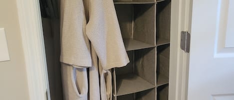 A walk-in closet with hanging robes and shelves.