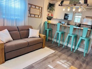 A cozy living room with a brown sofa and teal chairs, a kitchen with white cabinets, and a sign that reads 'Cottage'. - Blue Willow Country Cottage (Abilene)