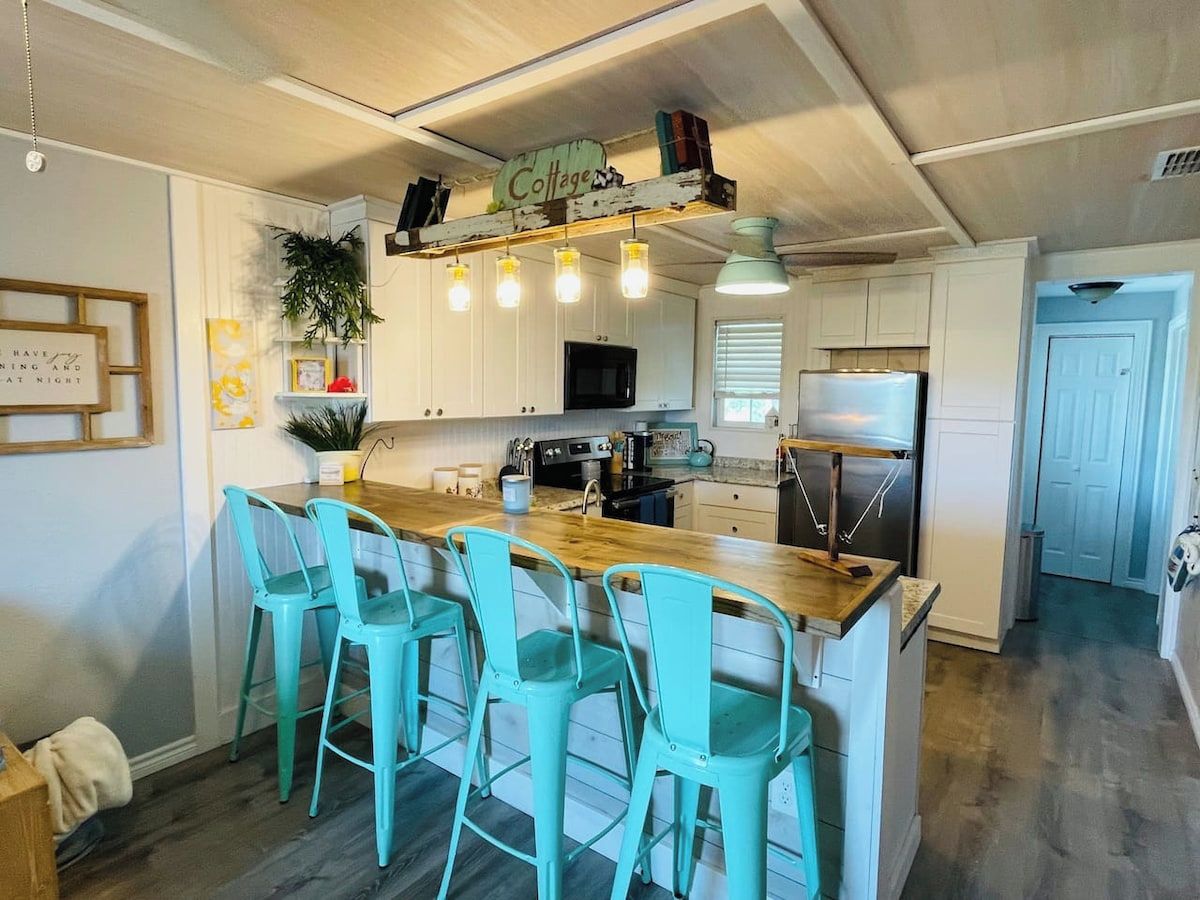 Una cocina con una isla de madera, taburetes de bar turquesa y un letrero que dice 'Cottage'.