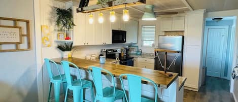 Una cocina con una isla de madera, taburetes de bar turquesa y un letrero que dice 'Cottage'.