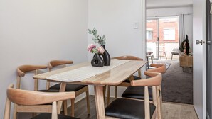 A dining area with a wooden table and chairs, a vase with flowers, and a view of the outside. - Cosy & Convenient Place in Inner West Area (no parking) (Strathfield)