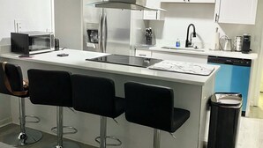 Et moderne køkken med en central ø, barstole, rustfrit stål hvide skabe.