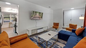En moderne stue med en sofa, et sofabord og et fjernsyn monteret på væggen.