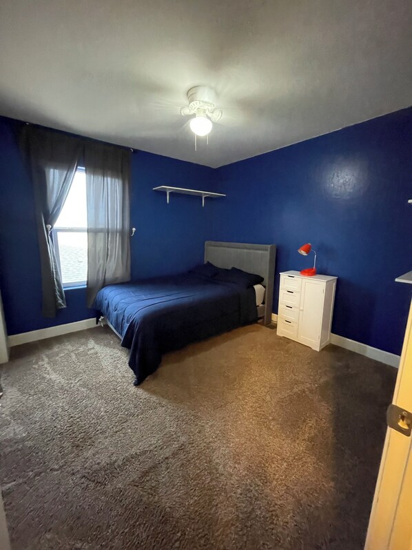 A bedroom with a bed, a nightstand, a dresser, a ceiling fan, and a window with curtains. - Spacious 4-bedroom house in charming Hobbs with AC, WiFi (Hobbs)