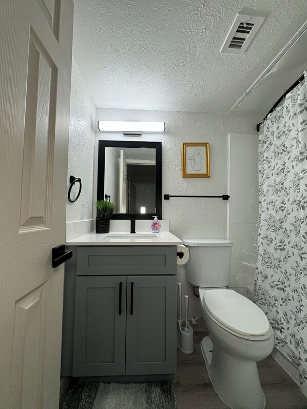 Une salle de bain avec un lavabo blanc, un miroir, des toilettes et un rideau de douche.