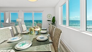 A dining area with a view of the ocean, wicker furniture, and a clock on the wall.