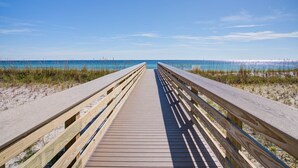 A wooden boardwalk leading to a beach with clear blue water and a clear sky.