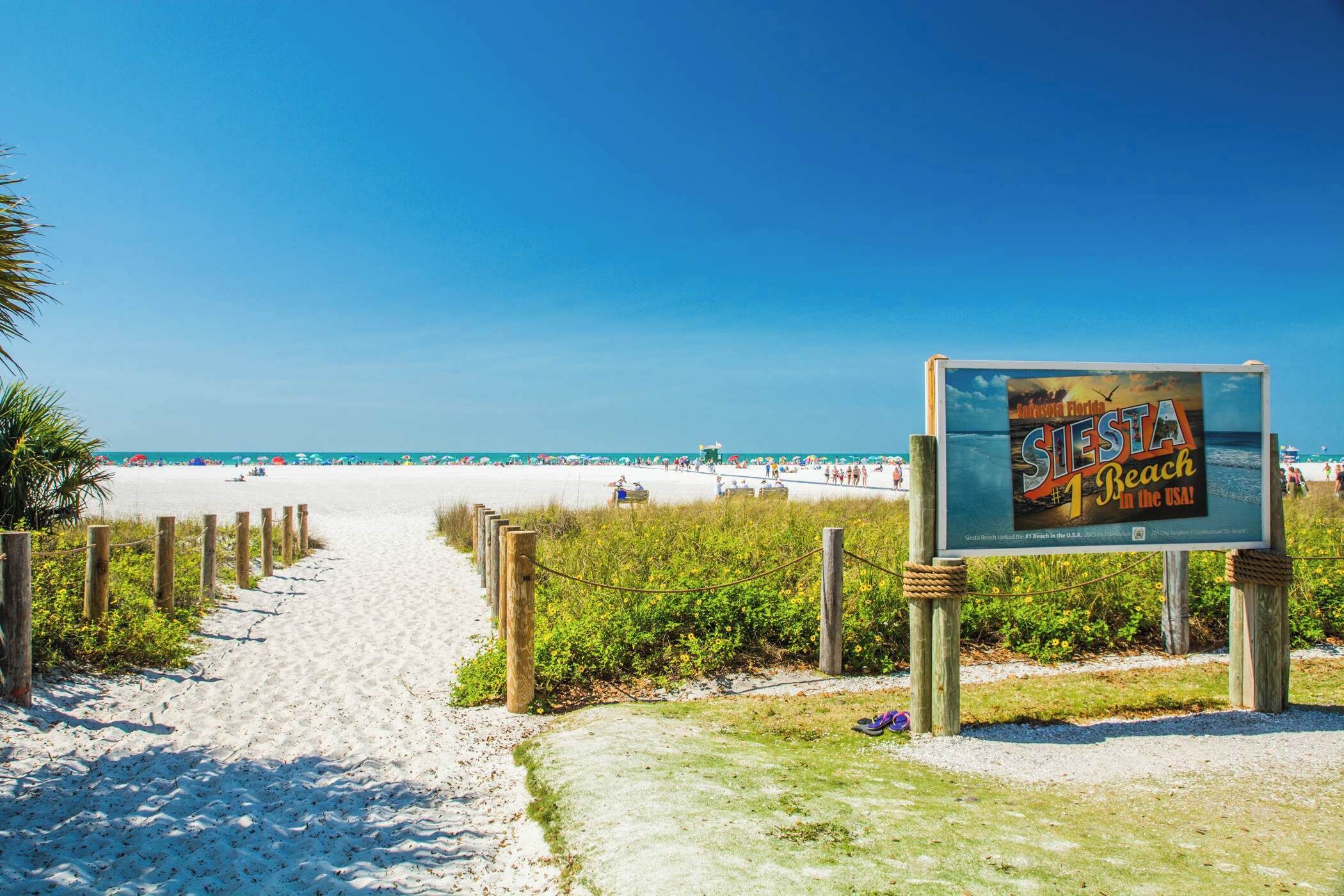 Een strandpad dat uitkomt op een zandstrand, met een bord waarop het strand wordt aangekondigd.