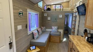 A compact, modern interior with a loft bedroom, a seating area with a laptop, and a kitchenette. - The Mermaid at Tiny House Siesta (Sarasota)