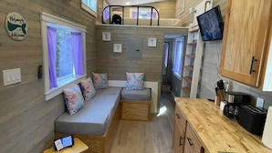 A compact, well-lit interior with a bunk bed, seating area, kitchenette, and a television. - The Mermaid at Tiny House Siesta (Sarasota)