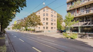 Katu, jossa kulkee raitiovaunukiskot, rakennus, jossa on useita ikkunoita, ja pyörä, joka on pysäköity jalkakäytävälle.