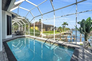 A swimming pool with a glass enclosure, a patio with outdoor furniture, and a view of a marina and houses in the background. - Spacious waterfront Oasis with heated pool. (Marco Island)