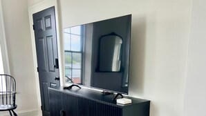 A modern living room with a black entertainment unit, a flat-screen TV, and a wooden floor. - Modern Suite on the River (Port Hope)