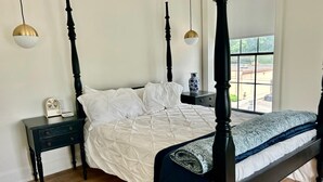 A four-poster bed with a quilted white duvet, a dark wooden nightstand with a radio, and a vase on the nightstand. - Modern Suite on the River (Port Hope)