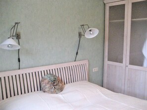 A bedroom with a white bed, a striped headboard, two wall-mounted lamps, and a wardrobe with a glass door. - Close to the sea, quiet location, pool and sauna - Reethaus Göhren FeWo 01 (Göhren)