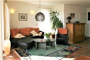 Un salon avec un canapé noir, une table basse ronde, une plante en pot, un meuble en bois et un luminaire suspendu.