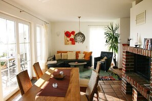 A spacious living room with a sofa, chairs, a dining table, and a fireplace. - Close to the sea, quiet location, pool and sauna - Reethaus Göhren FeWo 01 (Göhren)