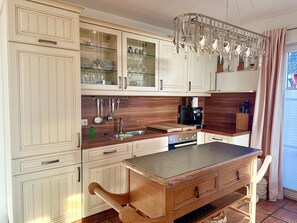 A kitchen with wooden cabinets, a sink, a coffee maker, and a hanging utensil rack. - Close to the sea, quiet location, pool and sauna - Reethaus Göhren FeWo 01 (Göhren)