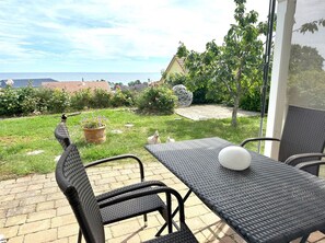 A patio with a table and chairs, a view of the sea, and a garden with various plants and a spherical sculpture. - Close to the sea, quiet location, use of swimming pool and sauna - Reethaus Göhren FeWo 01 (Göhren)